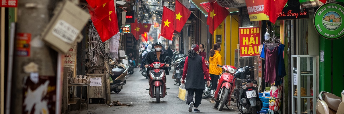 Hanoi Vietnam - Jan 30 2023: People go about daily life under Vietnamese flags in a narrow residential alleyway called Kham Thien Market in Hanoi, Vietnam.