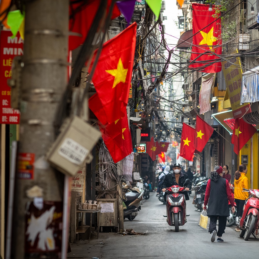 Hanoi Vietnam - Jan 30 2023: People go about daily life under Vietnamese flags in a narrow residential alleyway called Kham Thien Market in Hanoi, Vietnam.