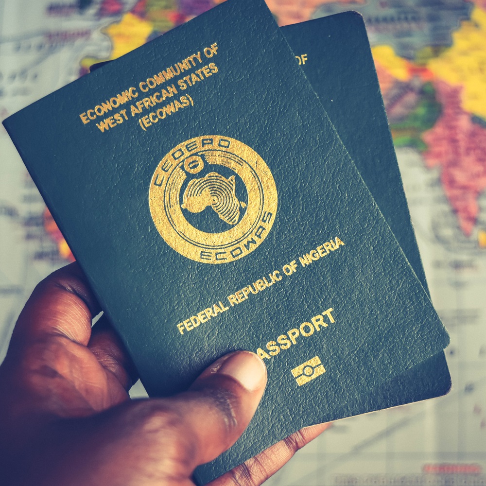 Ecowas passport in African hand, African holding two Green Nigerian Passports with map in the background