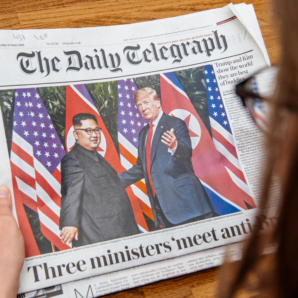 PARIS, FRANCE - JUNE 13, 2018: Woman reading The Daily Telegrpah newspaper in the office showing on cover U.S. President Donald Trump meeting North Korean leader Kim Jong-un in Singapore