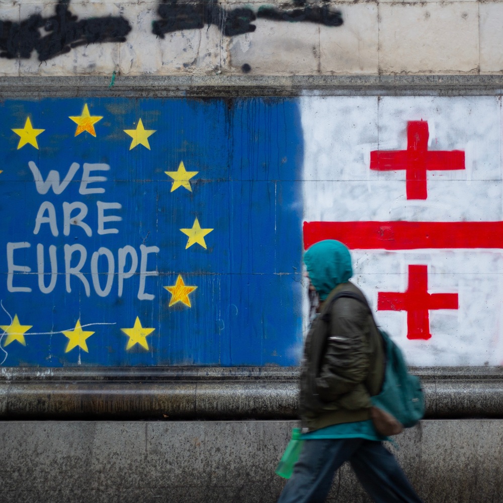 Tbilisi, Georgia - November 25, 2024: People out of focus near text We are Europe, EU and Georgian flag, cross, yellow star on blue house wall. Peaceful protest against result of parliament election