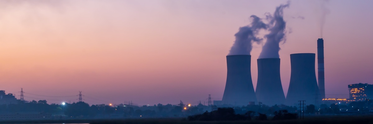 Coal powered thermal power plant. Chimney emitting smoke and cooling tower emitting steam. The lake near the electricity generating power plant showing reflections.