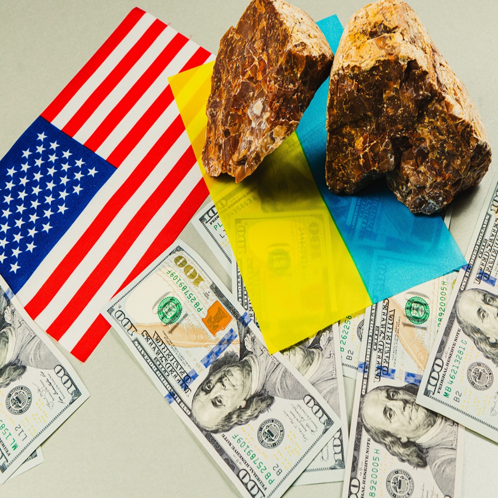 The image displays mineral rocks alongside US currency and flags of Ukraine and the USA, highlighting the complex relationship involving economics, power, and resources.