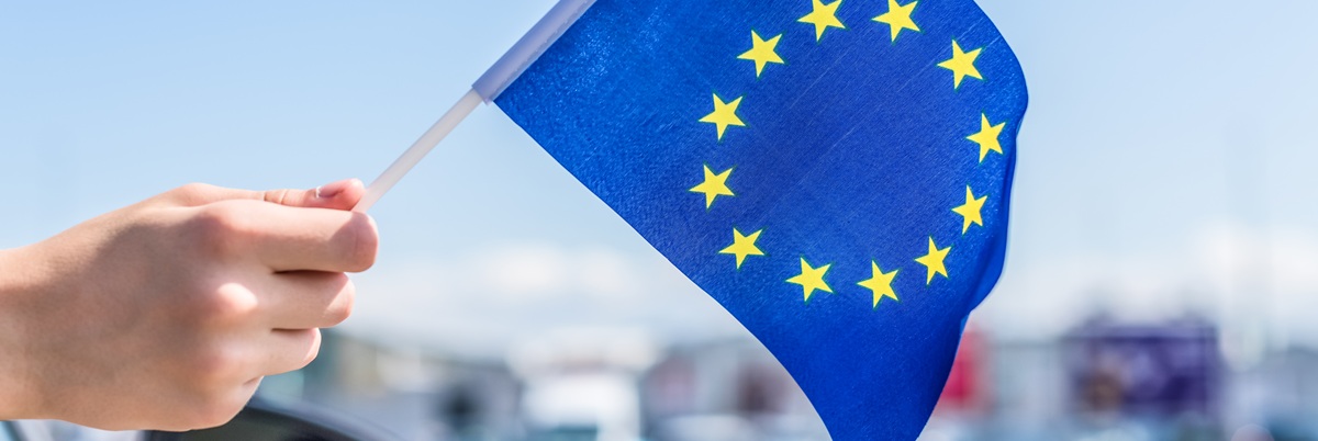 Boy holding Europe or European(EU) Flag from the open car window on the parking of the shopping mall. Concept