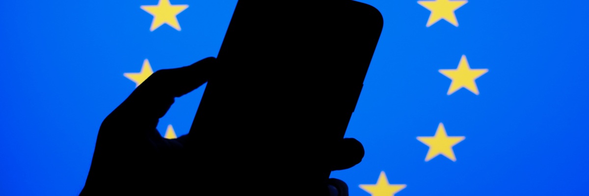Silhouette of a person holding a smartphone in front of the flag of The European Union (EU)